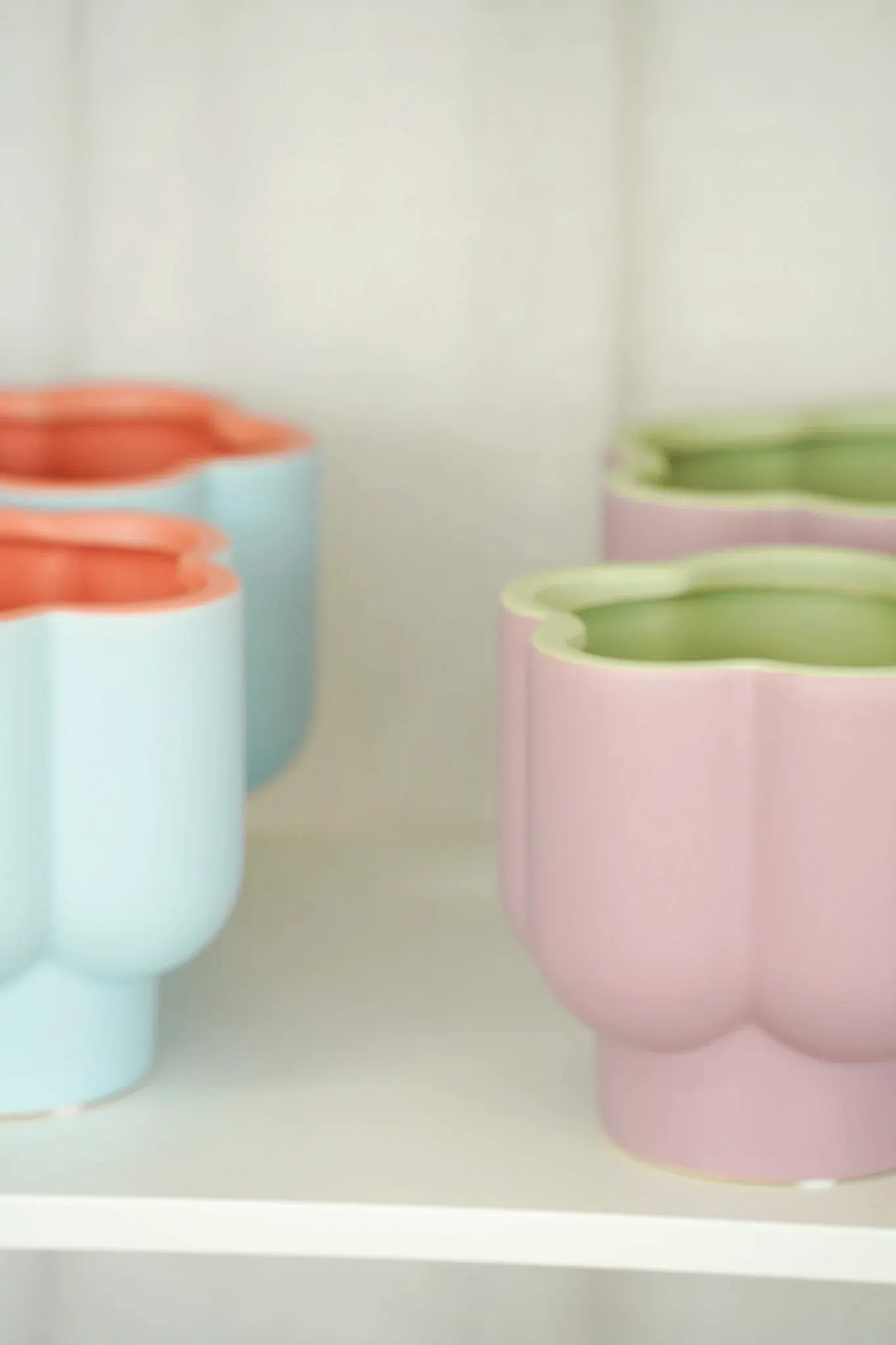 Pastel-colored flower-shaped pots in soft shades of blue, pink, and green displayed on a white shelf, showcasing a minimalist design.