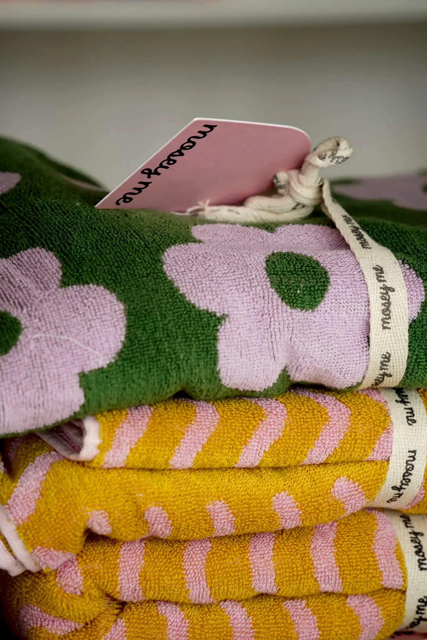 Brightly patterned towels by Mosey Me, featuring pink floral and yellow striped designs, neatly tied with branded cotton ribbons.